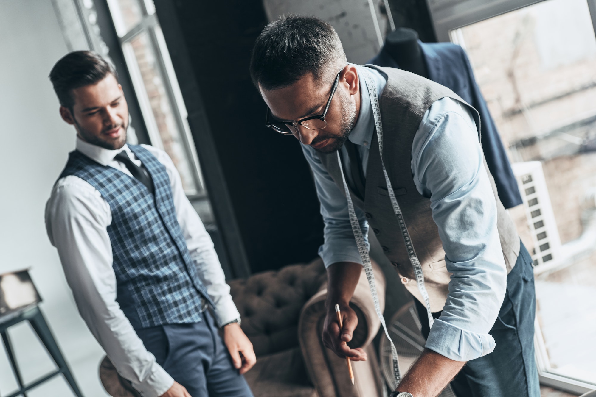 Order details. Two young fashionable men having a discussion while standing in workshop